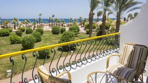 Een balkon met rieten stoelen, uitzicht op het strand, palmbomen en een heldere lucht.