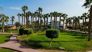 Een resort met een verzorgd gazon, palmbomen en een pad dat naar een gebouw met een rode dakbedekking leidt.