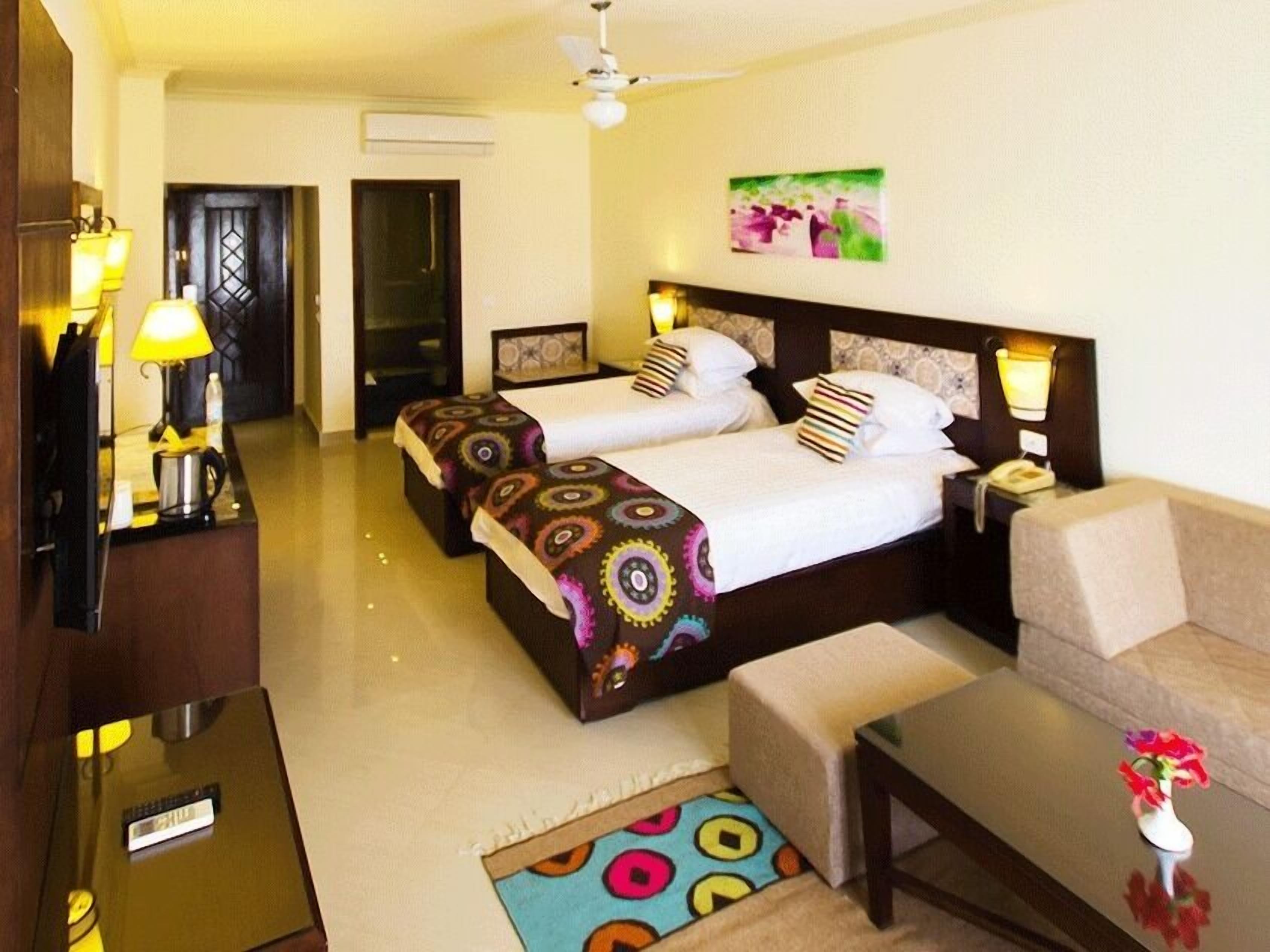Habitación de hotel con dos camas, un sofá, una mesa de centro, un televisor y un cuadro en la pared.