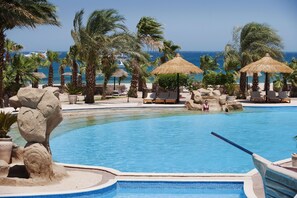 Zona de piscina con sillones de descanso, palmeras y vista al océano.