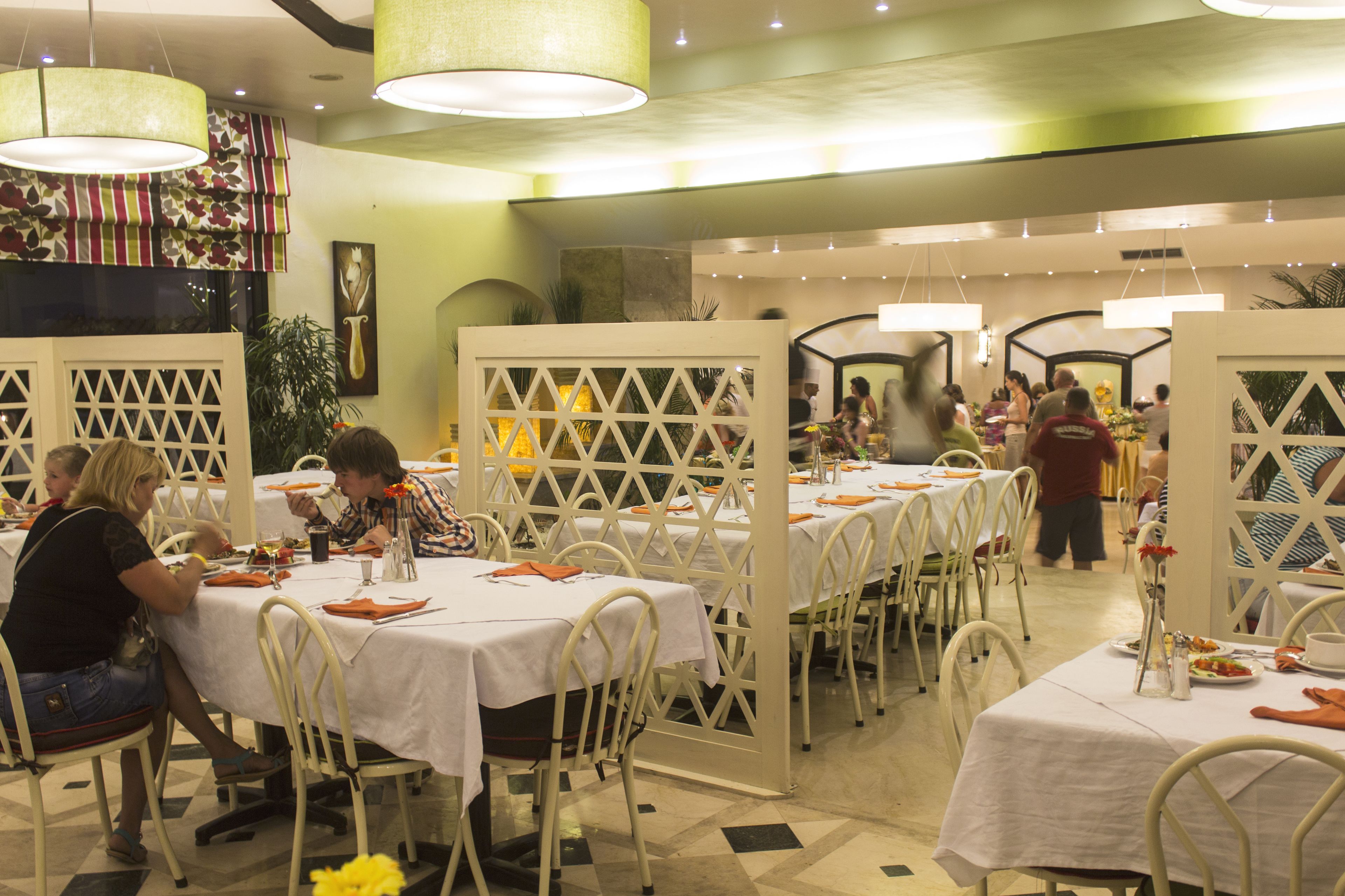 Un restaurante con manteles blancos, sillas blancas y una pared verde.