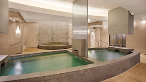 Un área de piscina interior moderna con dos piscinas separadas, una pared de piedra y un techo transparente.