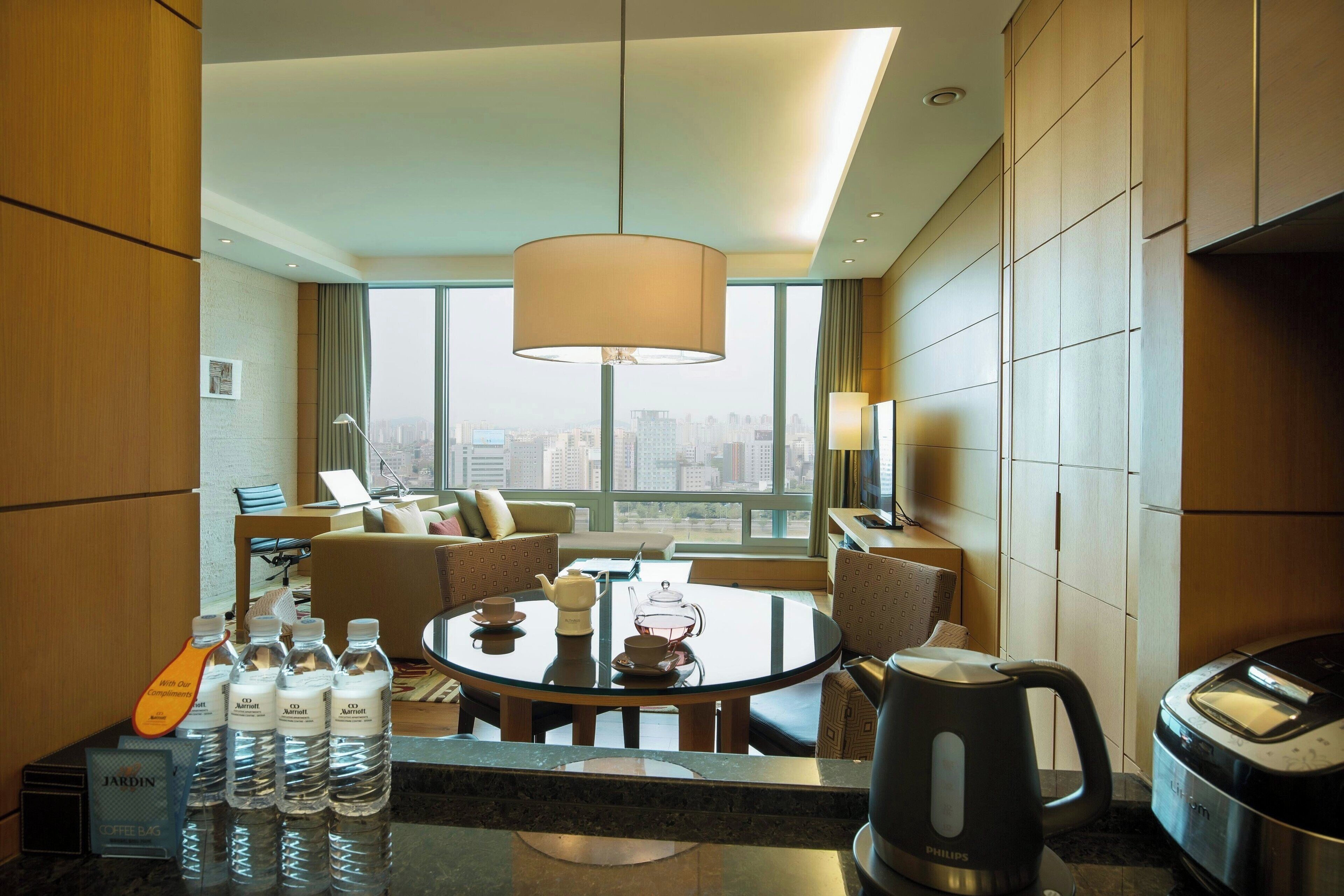 Una habitación de hotel moderna con zona de comedor, estación de café y vistas a la ciudad.