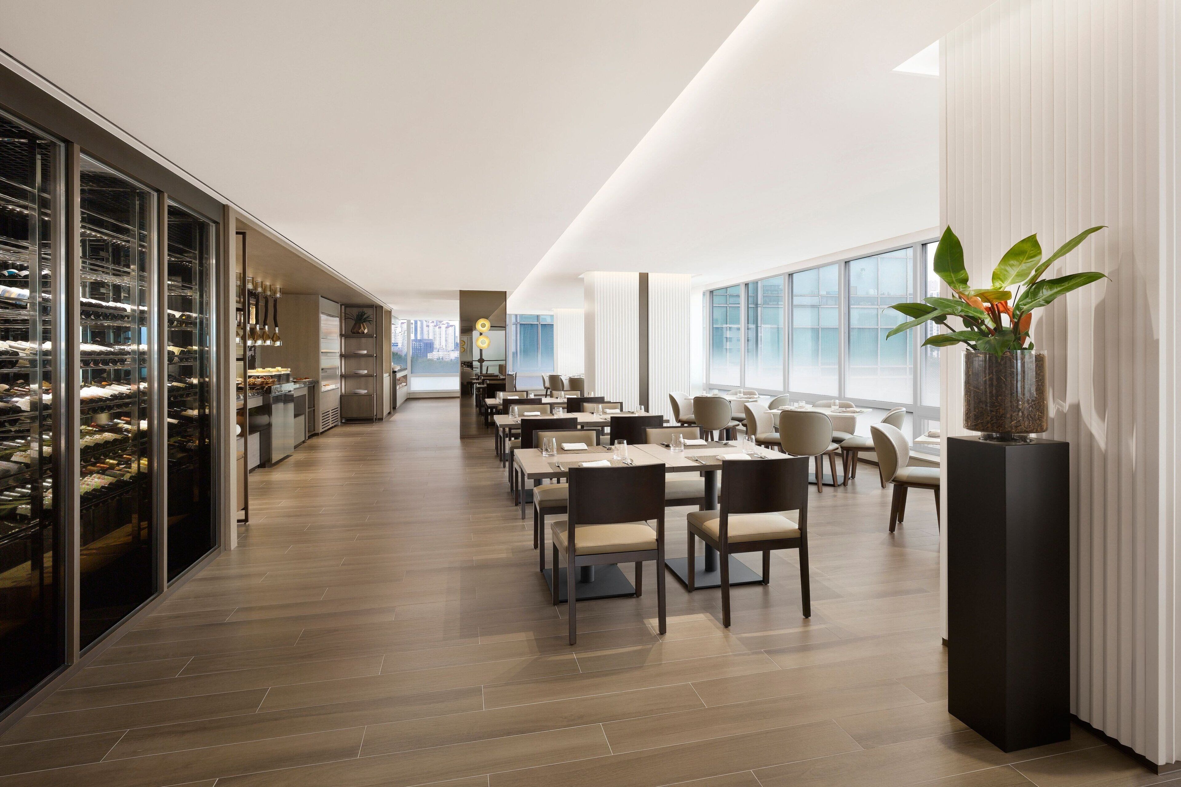 A modern dining area with long tables, chairs, and a large window providing a view of the city.