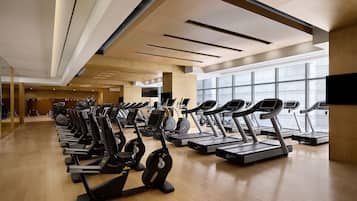 A gym with multiple treadmills and elliptical machines arranged in rows.