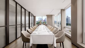 Una sala de conferencias moderna con una mesa larga dispuesta para una reunión, ventanas amplias que ofrecen vistas a la ciudad y un diseño minimalista.