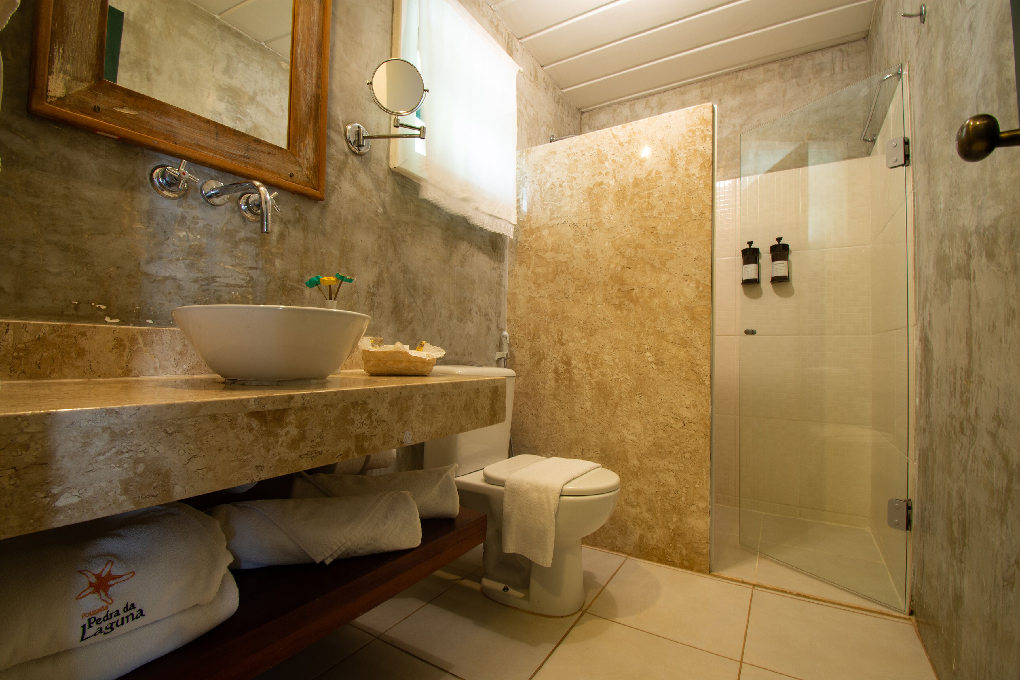A bathroom with a marble sink, a toilet, a glass-enclosed shower, and a towel rack.