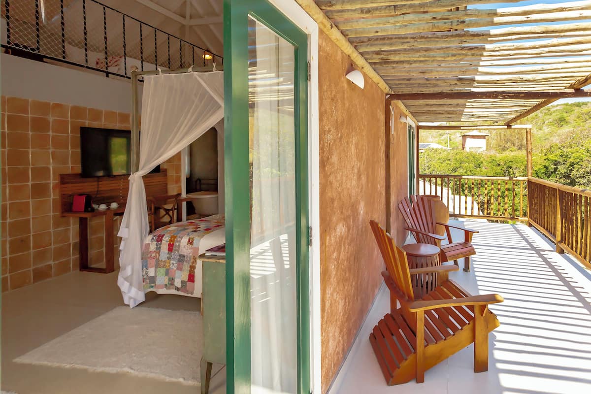 Un balcon avec une chaise en bois, un lit avec une courtepointe et un téléviseur posé sur une étagère.