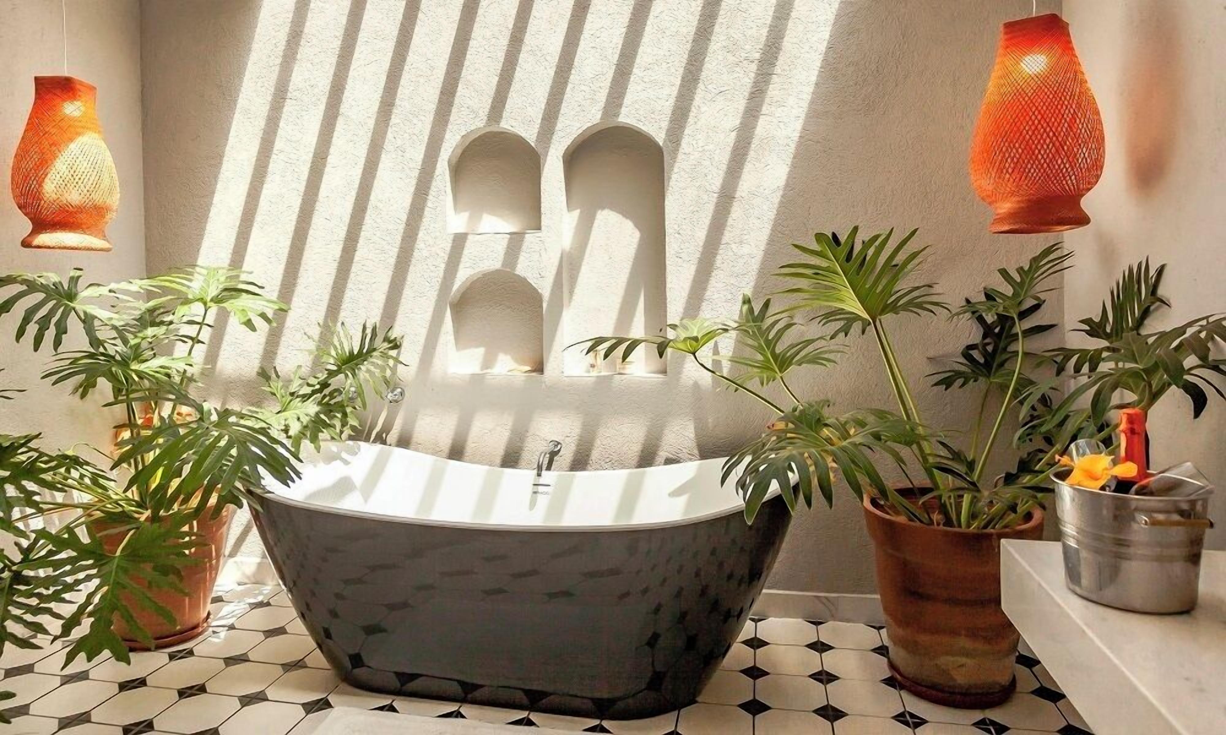 Un bany modern amb banyera autònoma, plantes en testos i aplics decoratius.