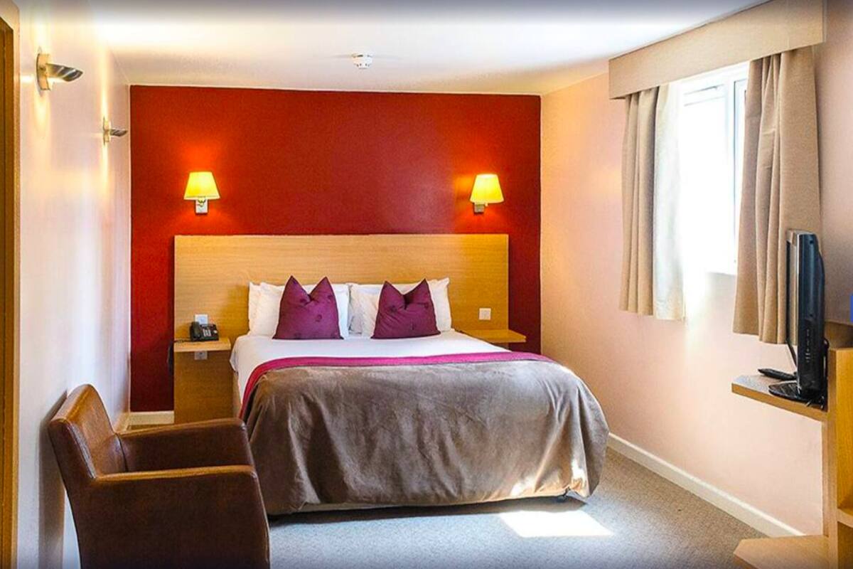 Quarto de hotel com uma cama grande, duas luminárias de cabeceira, televisão e uma cadeira.