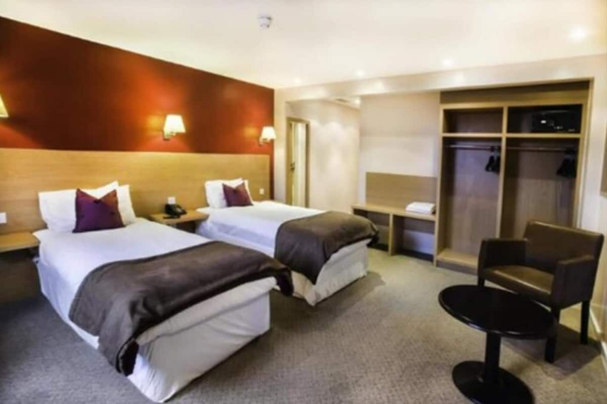 Quarto de hotel com duas camas, uma escrivaninha, uma cadeira e um guarda-roupa.