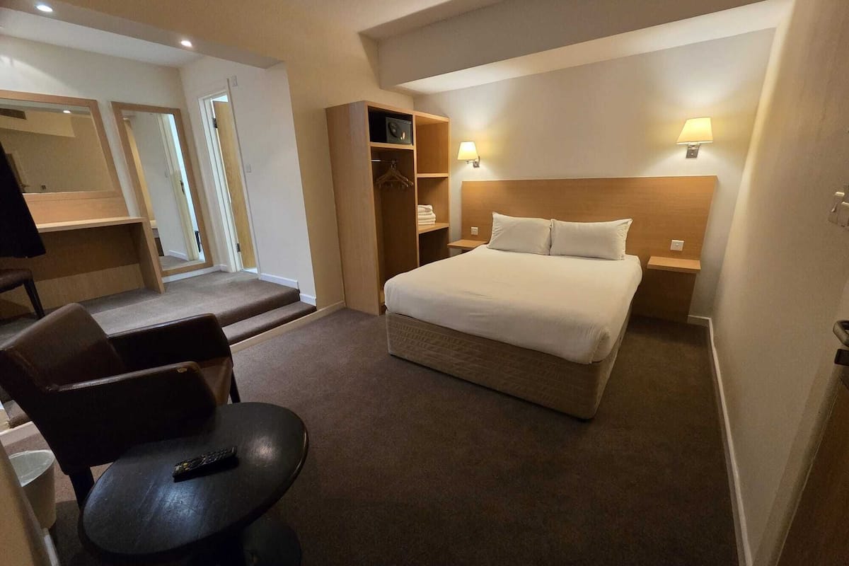 Quarto de hotel com cama, escrivaninha, cadeira, guarda-roupa e uma pequena mesa.