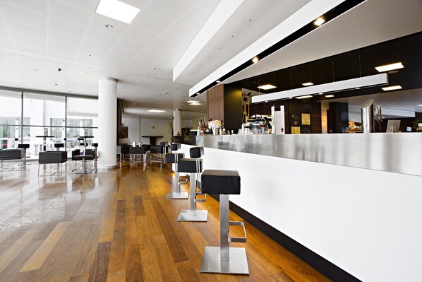 A modern bar area with a long counter, multiple stools, and a polished wooden floor.