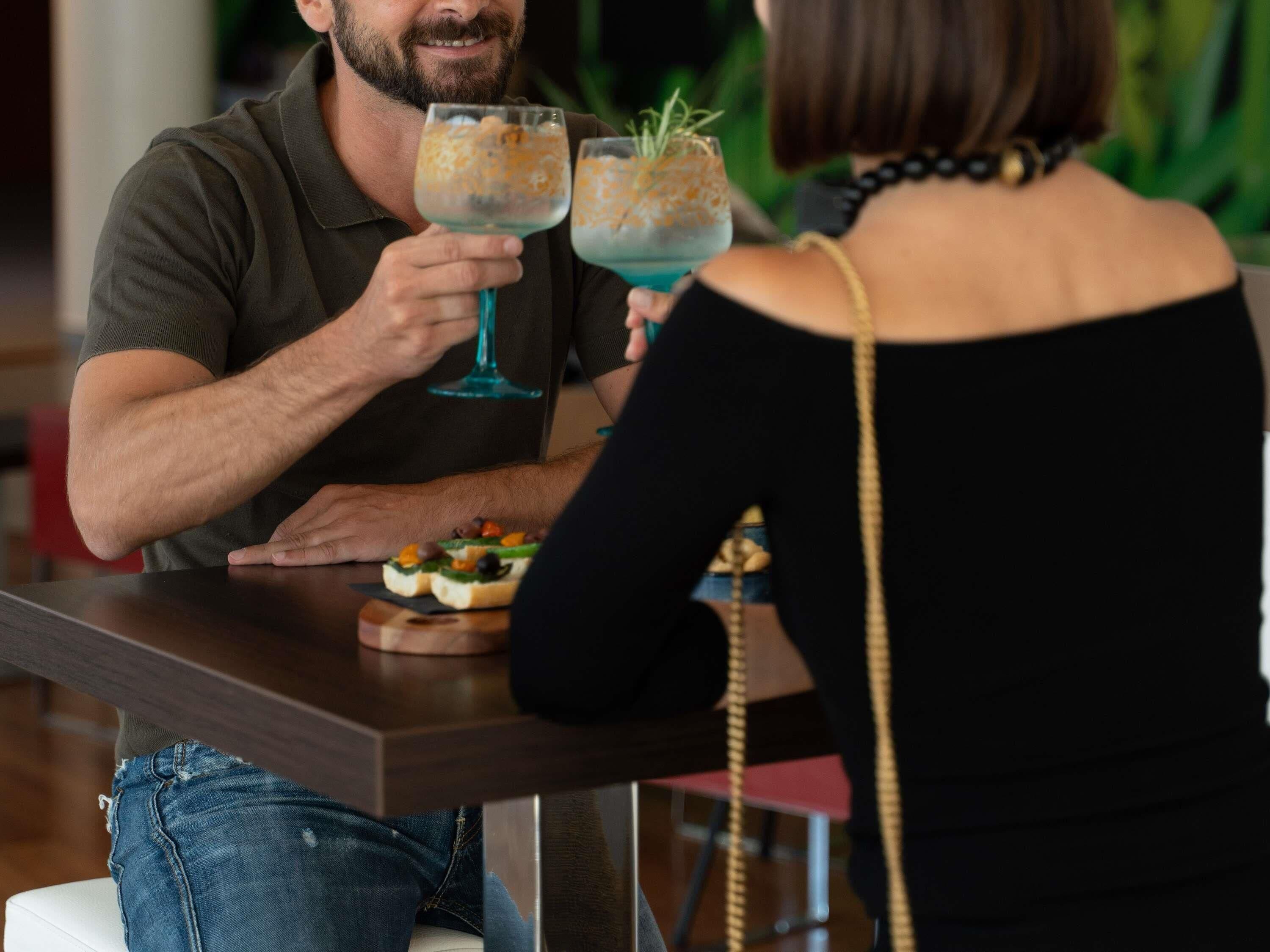 Un homme et une femme sont assis à une table, devant des boissons et des amuse-gueules.