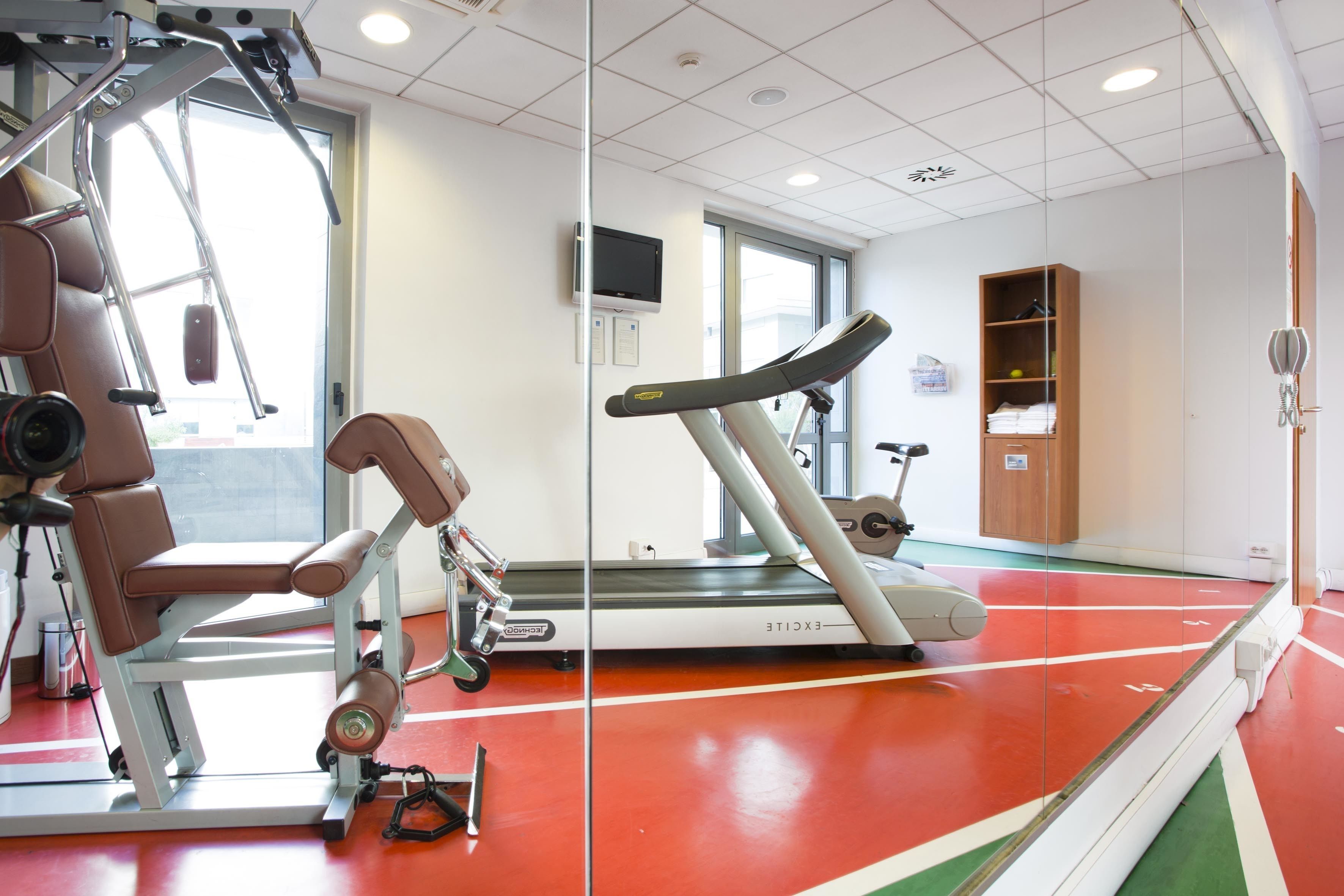 A gym with exercise equipment, a treadmill, and a mirrored wall.