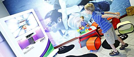 A child playing with toys in a room with a large poster of a person swimming and a Novotel sign.
