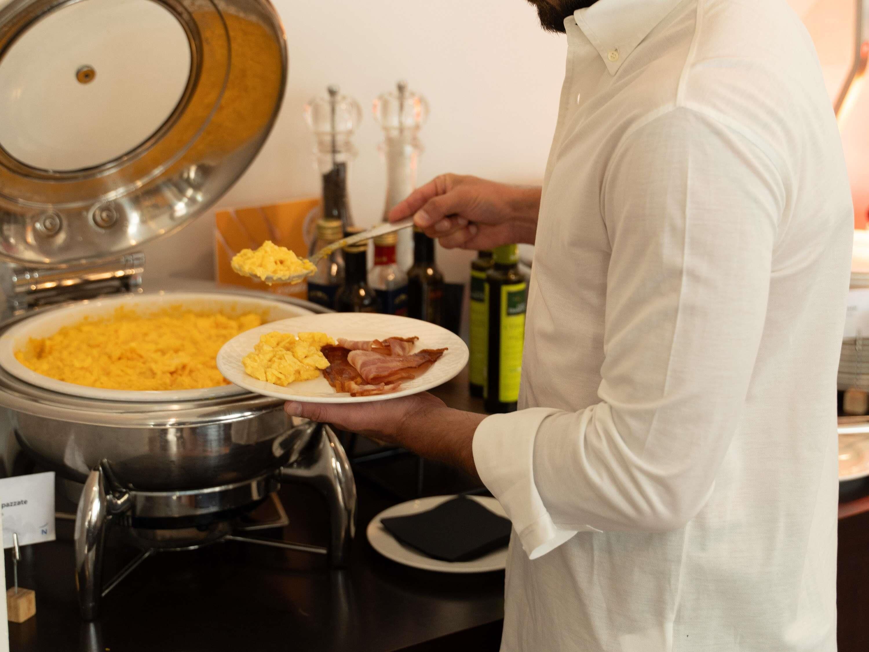 Une personne servant des œufs brouillés et du bacon dans une assiette.