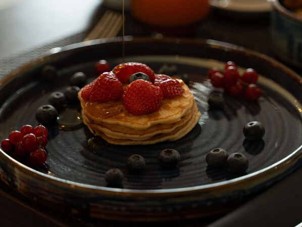 A stack of pancakes with berries and syrup on a plate.