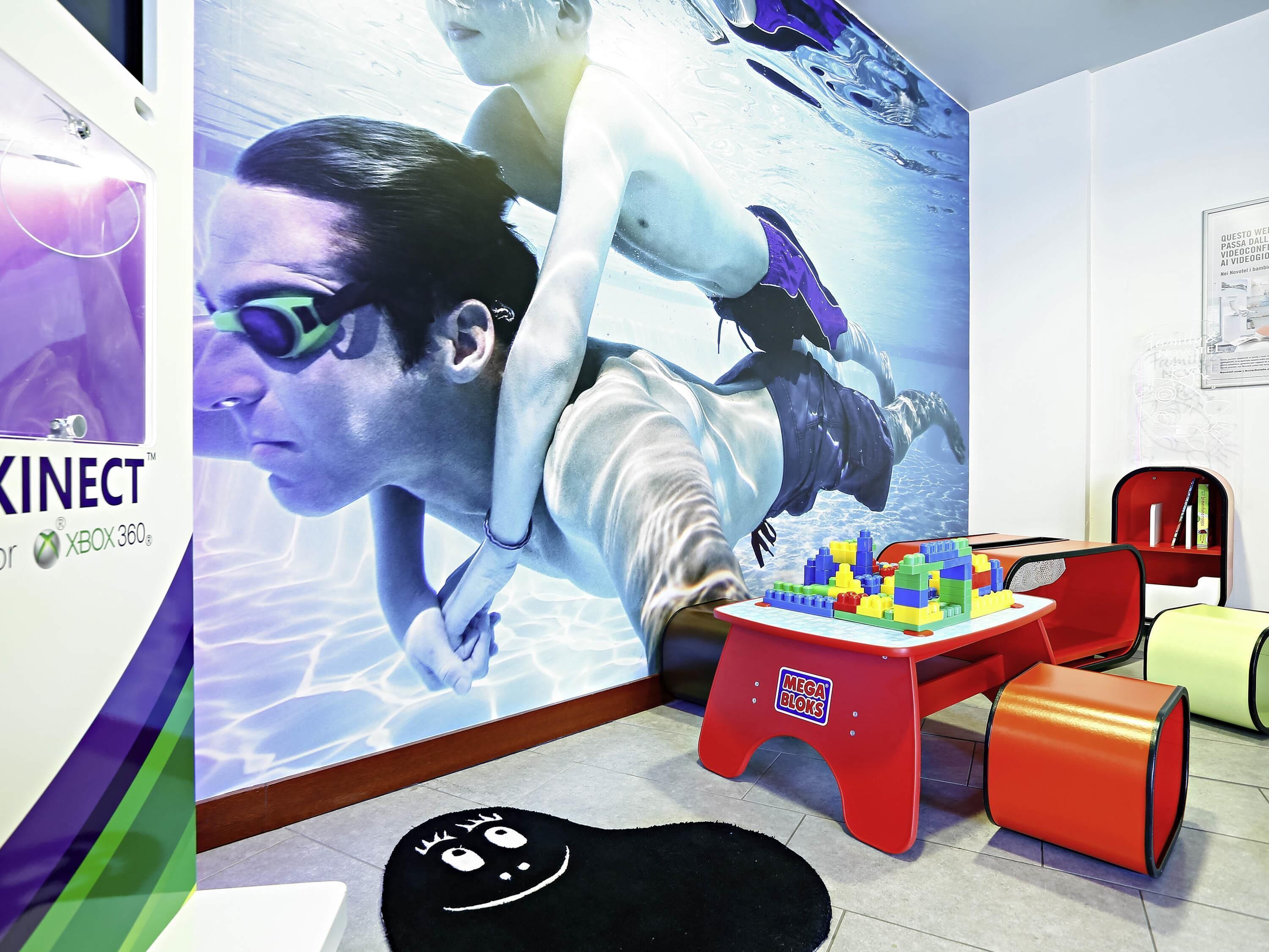 A room with a wall mural, a small table with building blocks, and a black rug with a face design.