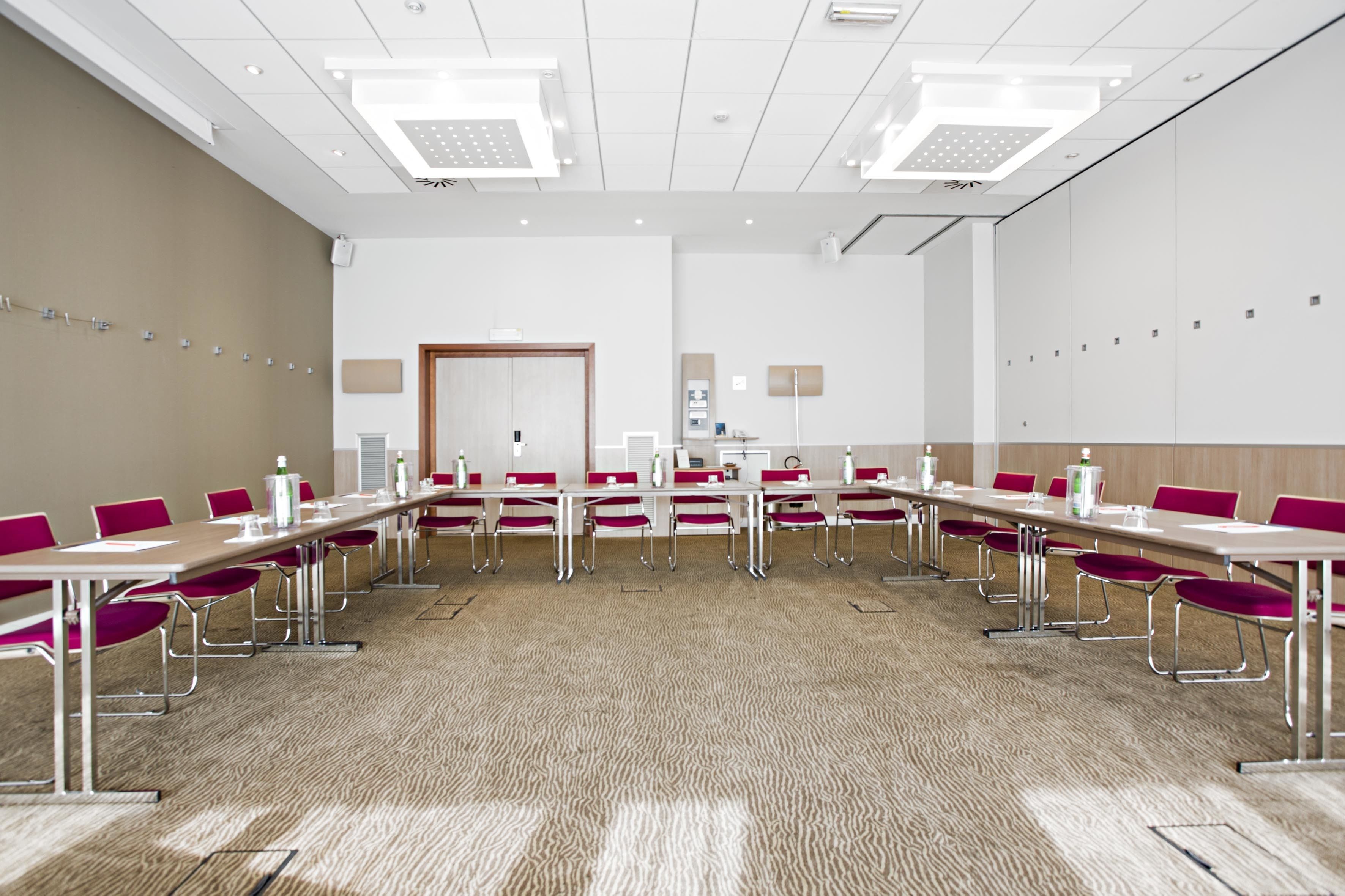 A conference room with a long table, red chairs, and white walls.
