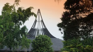 A modern building with a unique conical roof structure surrounded by lush greenery.
