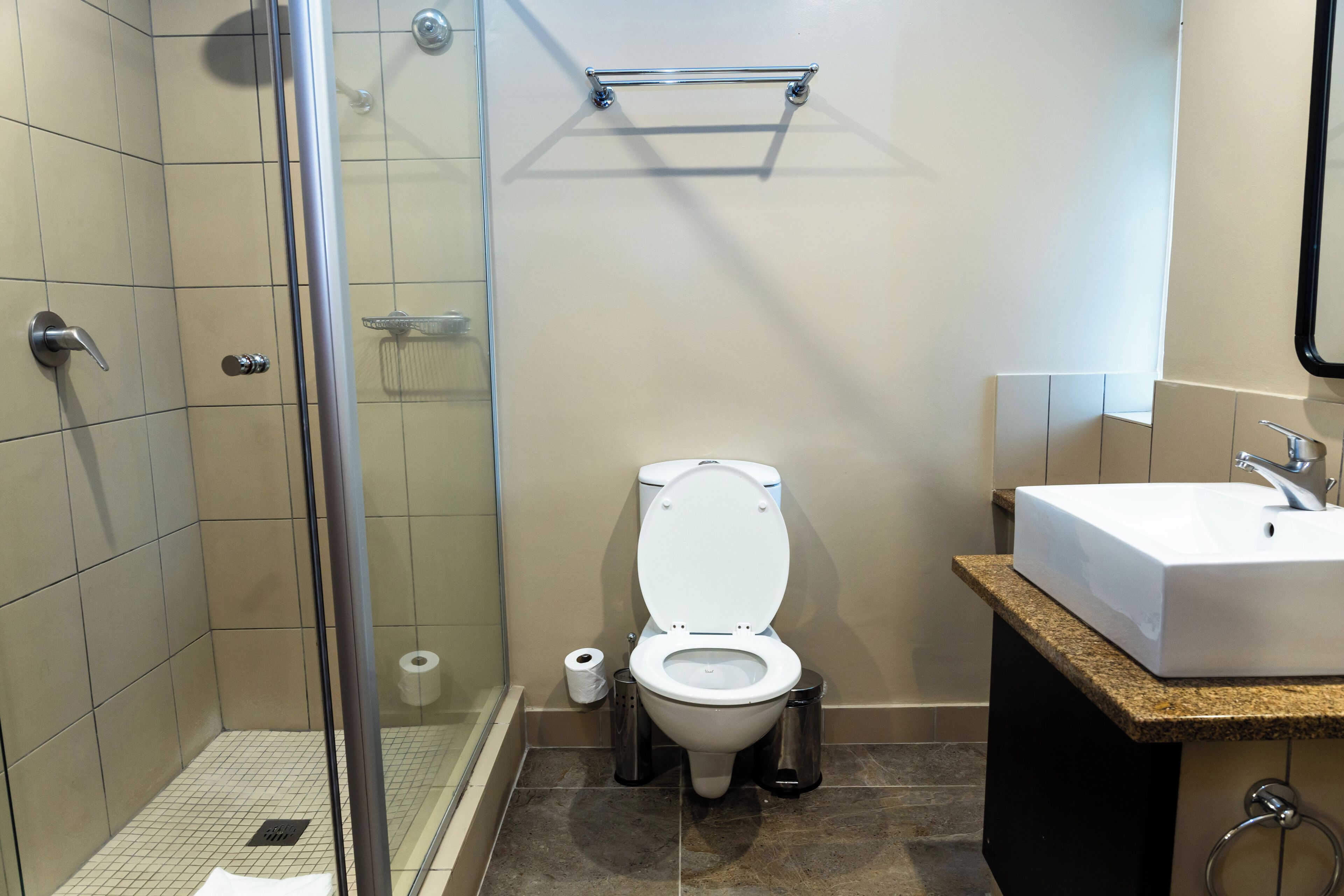 A bathroom with a glass-enclosed shower, a white toilet, and a sink with a granite countertop.