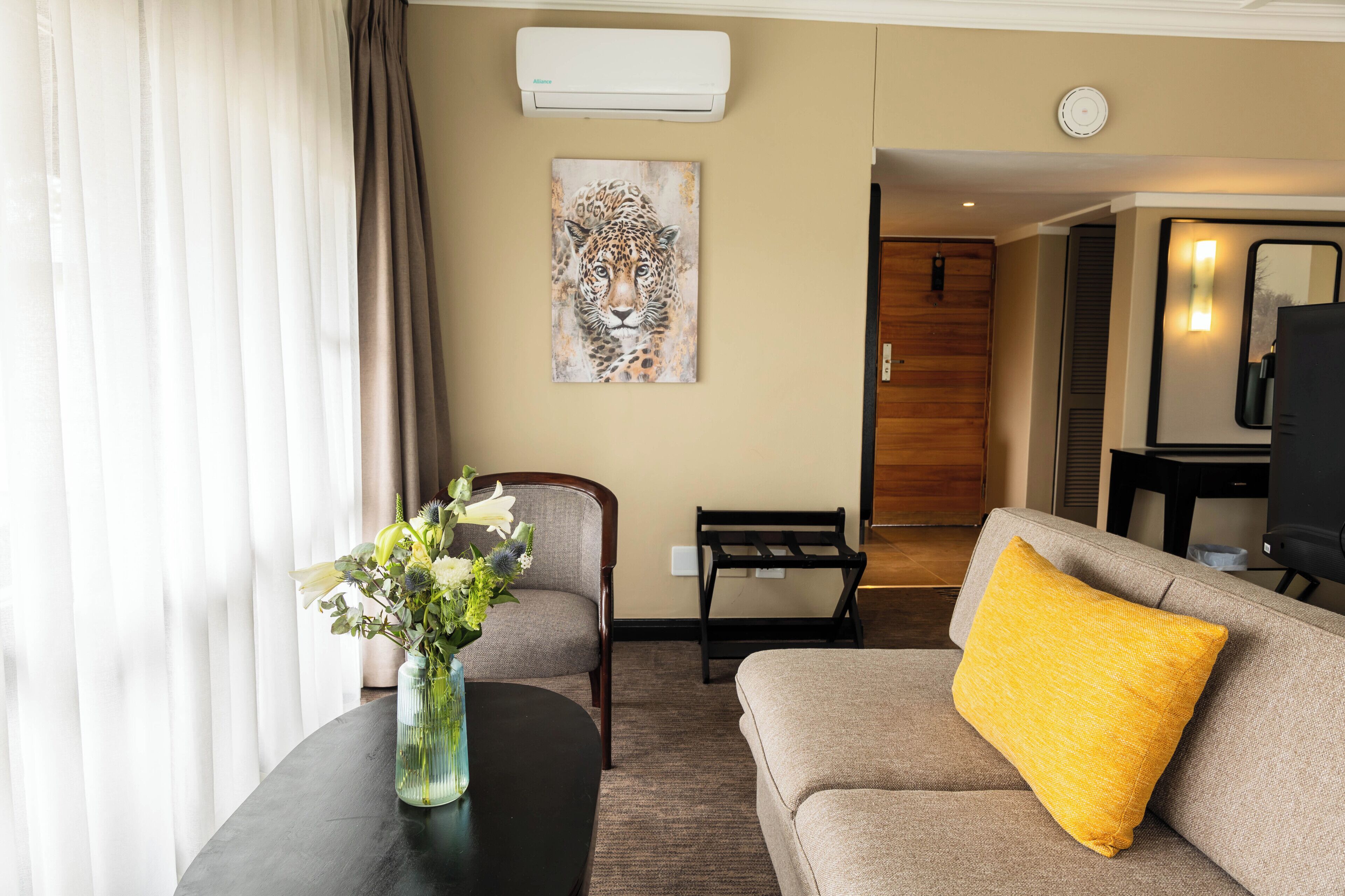 Un salón con un sofá, una mesa de centro con un jarrón de flores, un cuadro de un leopardo y una puerta de madera que da a otra habitación.
