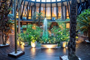 Un atrio circular con una fuente central, rodeado de diversas plantas y árboles en macetas.