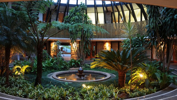 A lush indoor garden with a central fountain, surrounded by various tropical plants and a stone pathway.