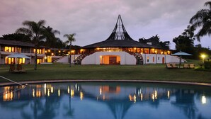 A resort with a pool, a large building with a unique roof, and palm trees.