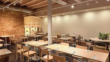 Un restaurante con paredes de ladrillo, mesas y sillas de madera, y un techo moderno con vigas y luminarias a la vista.