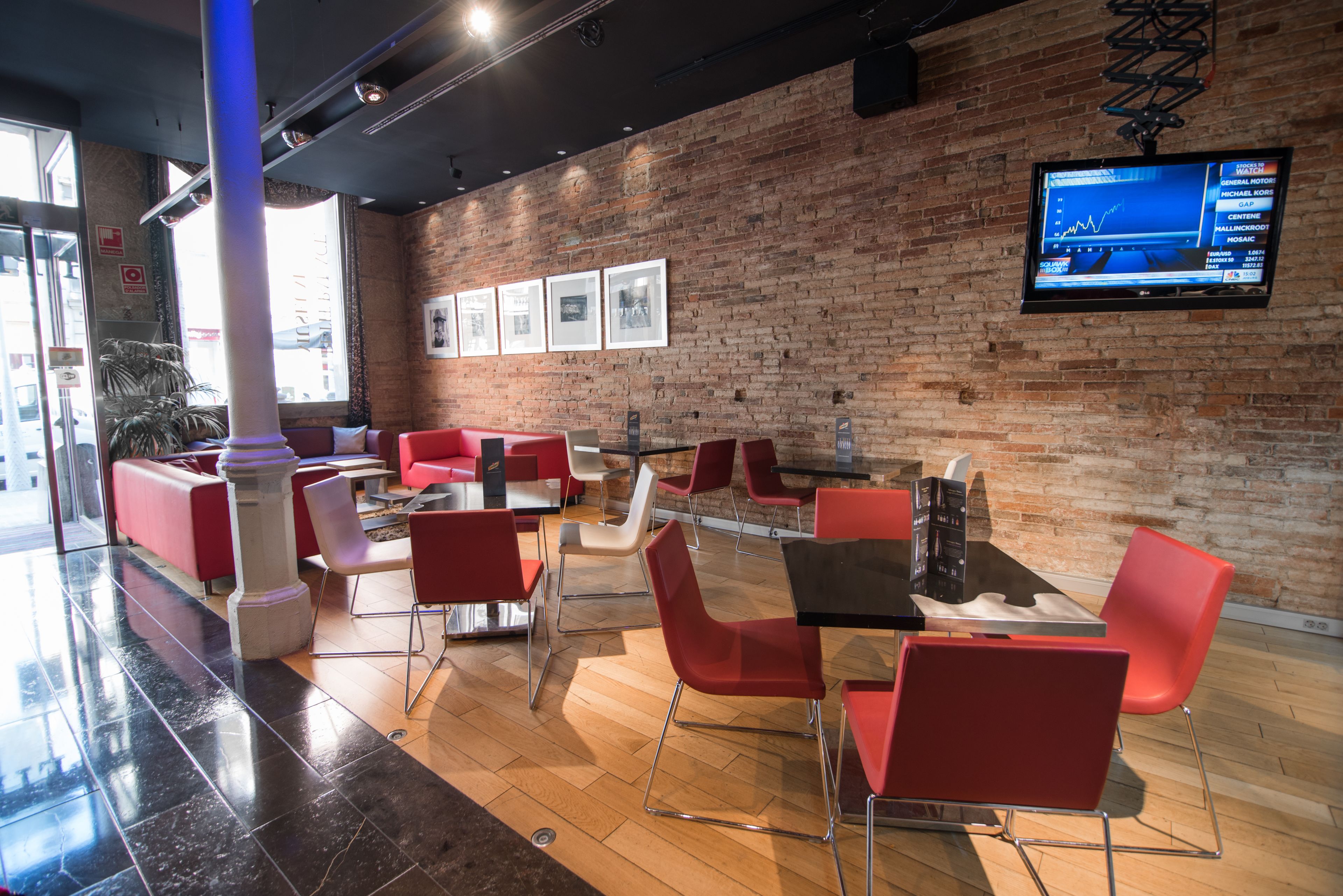 Een modern restaurant met rode en witte stoelen, een bakstenen muur en een televisie waarop een grafiek wordt weergegeven.