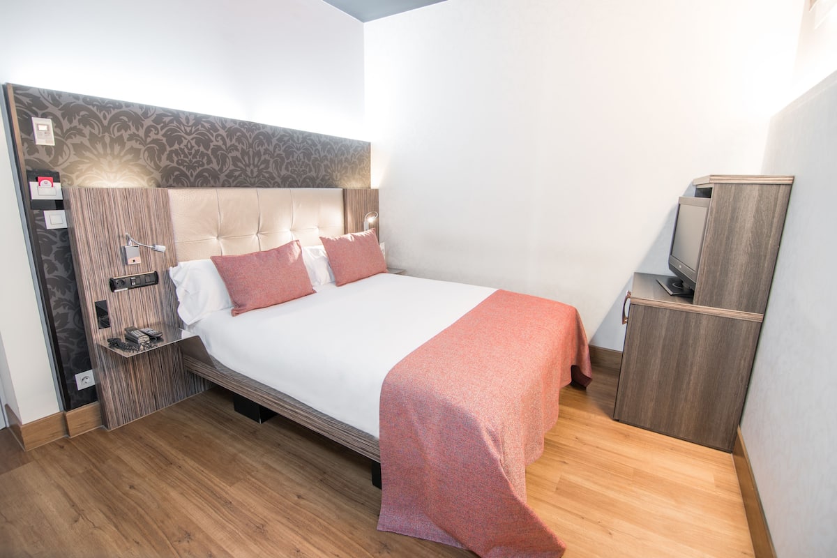 A neatly arranged hotel room with a large bed, a television, and a wooden cabinet.