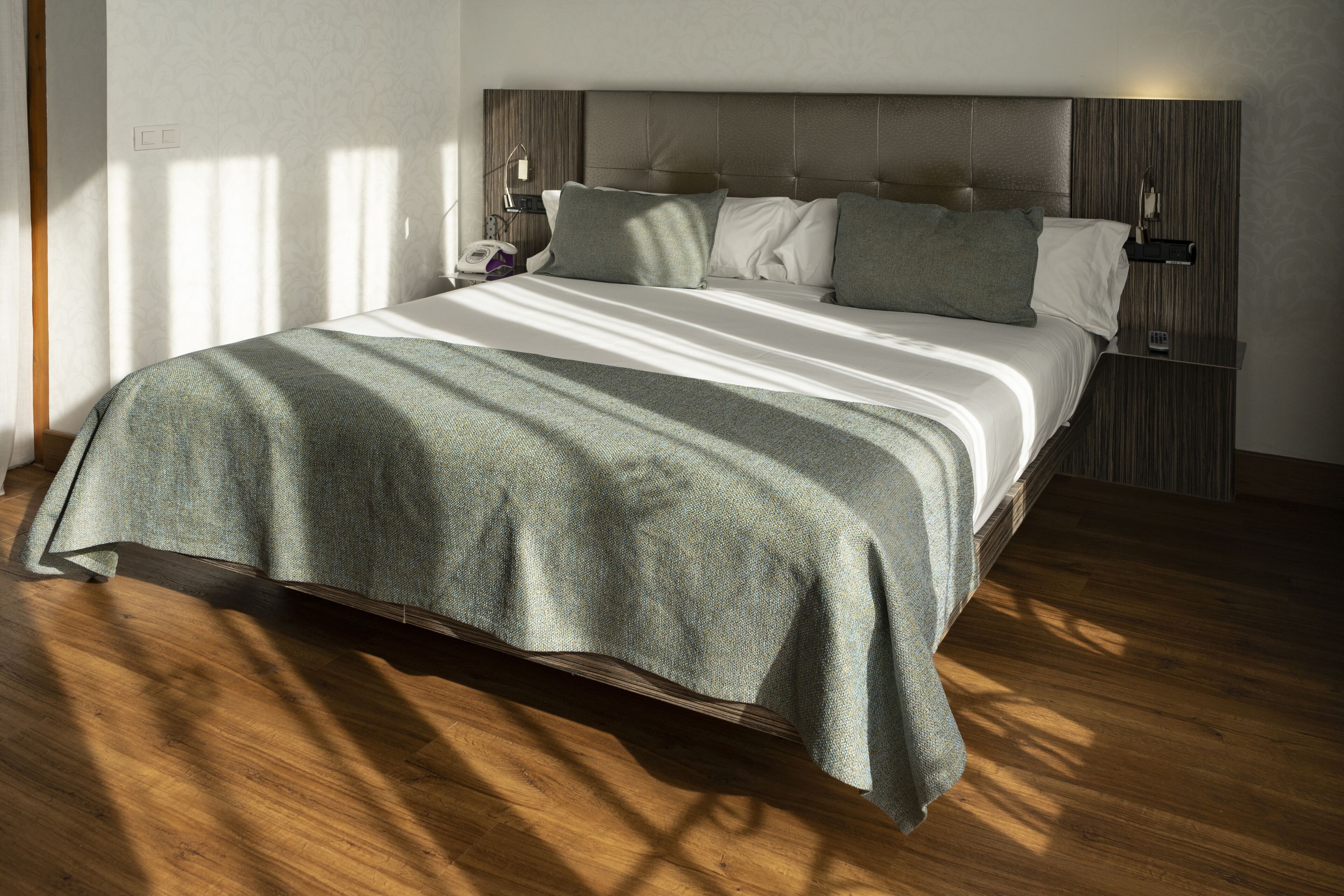 Una habitación de hotel moderna con una cama grande, piso de madera y una paleta de colores neutros.