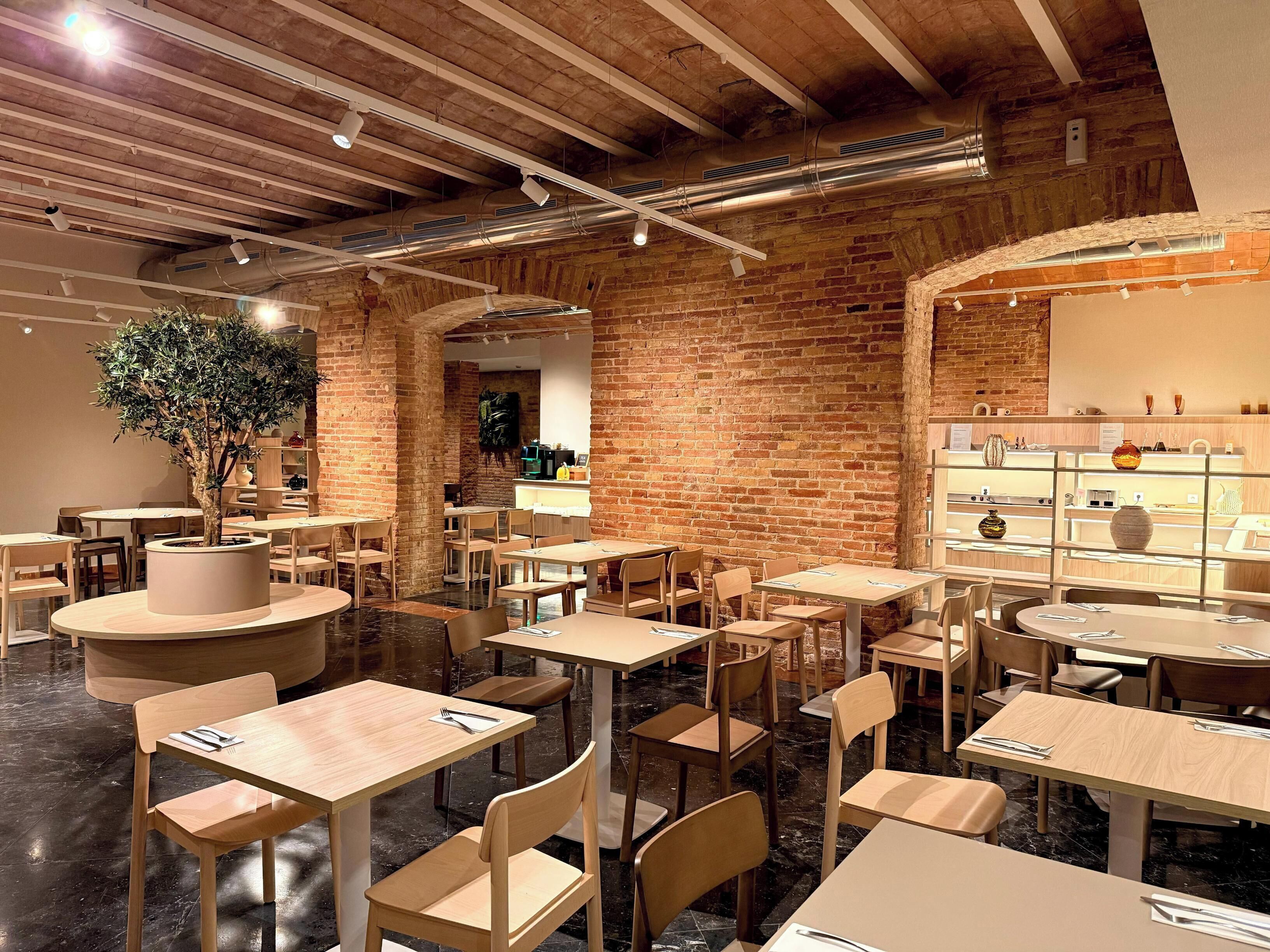 Un restaurante con paredes de ladrillo, mesas y sillas de madera, un árbol en maceta y una exhibición de jarrones.
