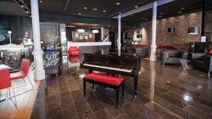A modern lobby with a grand piano, red seating, and a reception area. - Petit Palace Museum (Barcelona)