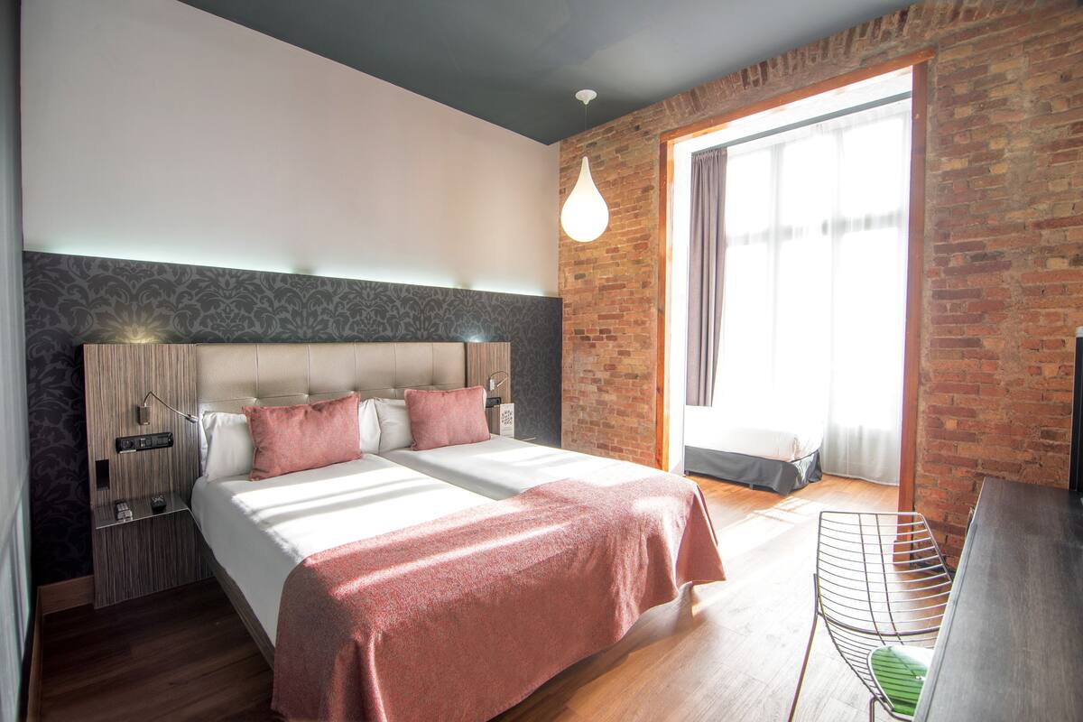 A modern hotel room with a large bed, a desk, and a brick wall.