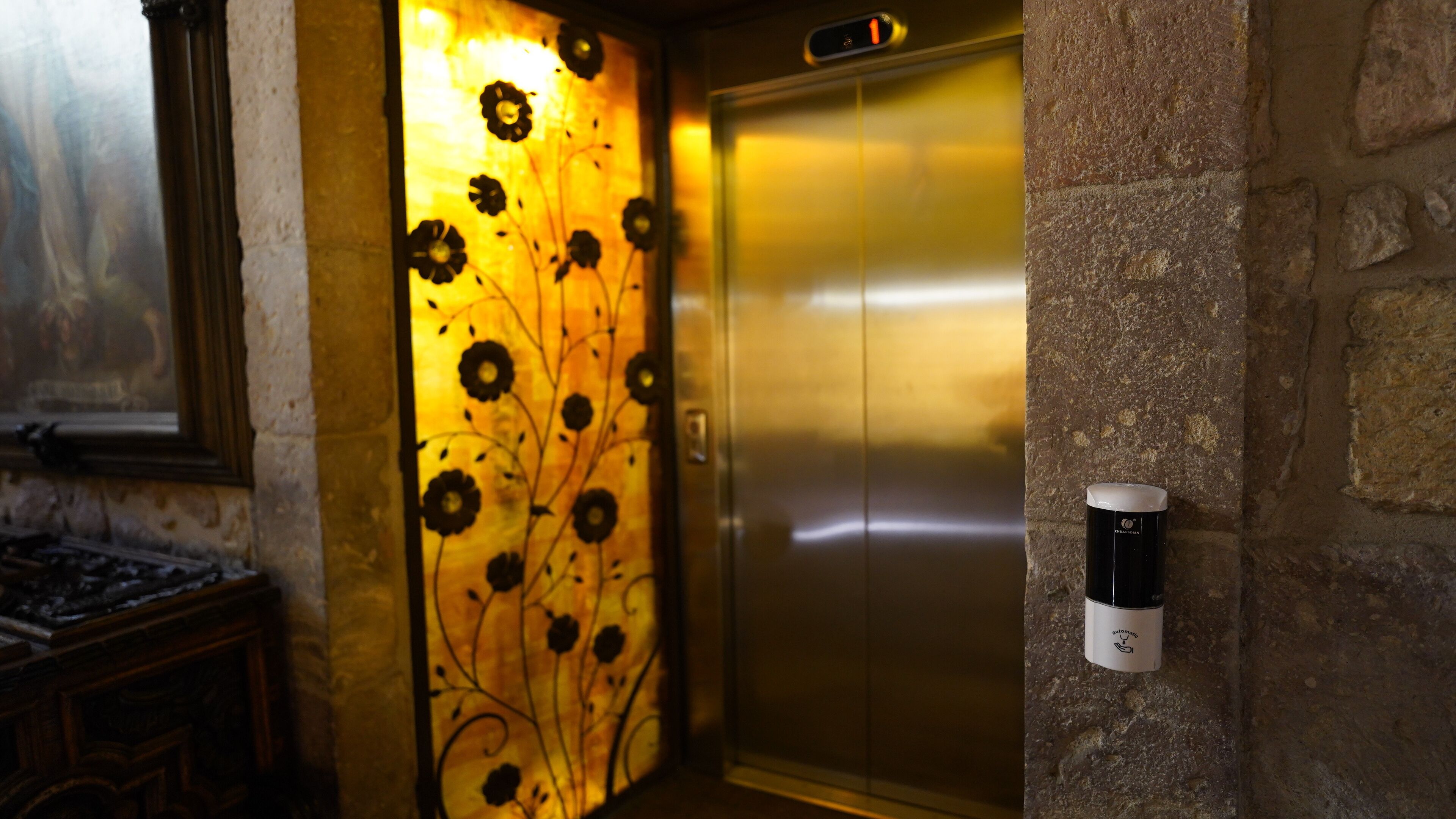 An elevator with a floral design on the wall, a stone wall, and a fire alarm on the right.