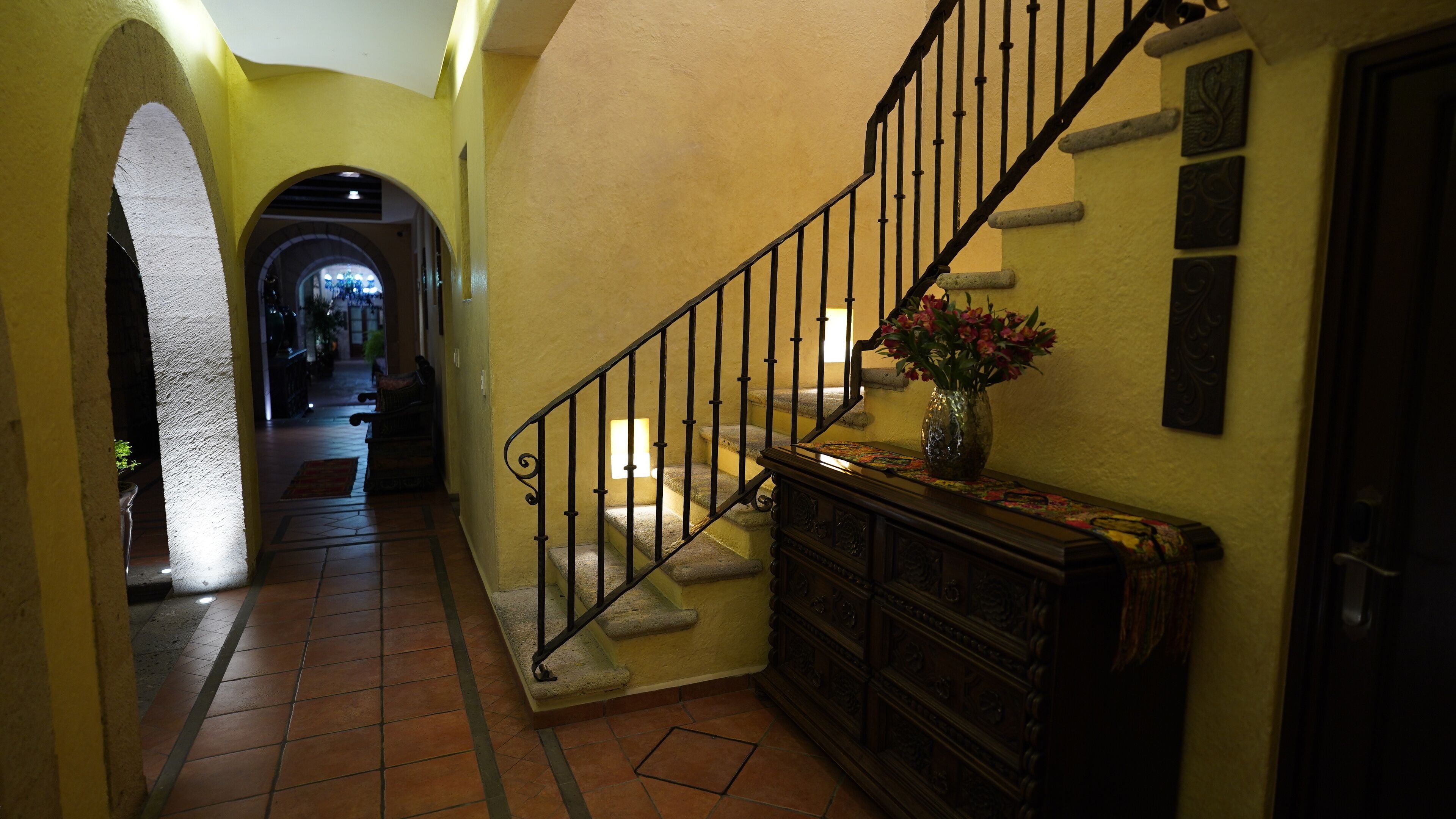 A hallway with a staircase, a vase with flowers, and a door.
