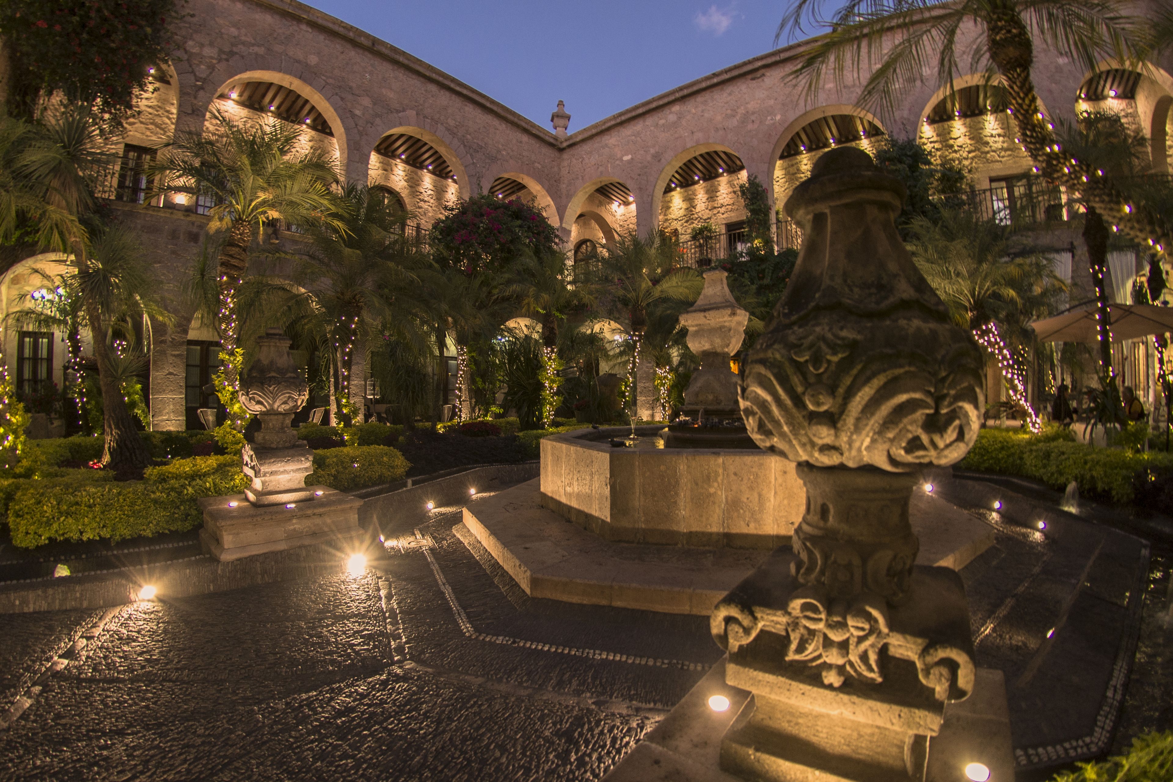 A courtyard with a fountain, palm trees, and stone architecture.