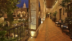 Un patio interior con columnas de piedra, suelo de baldosas y zonas de estar al aire libre con sillas y mesas.