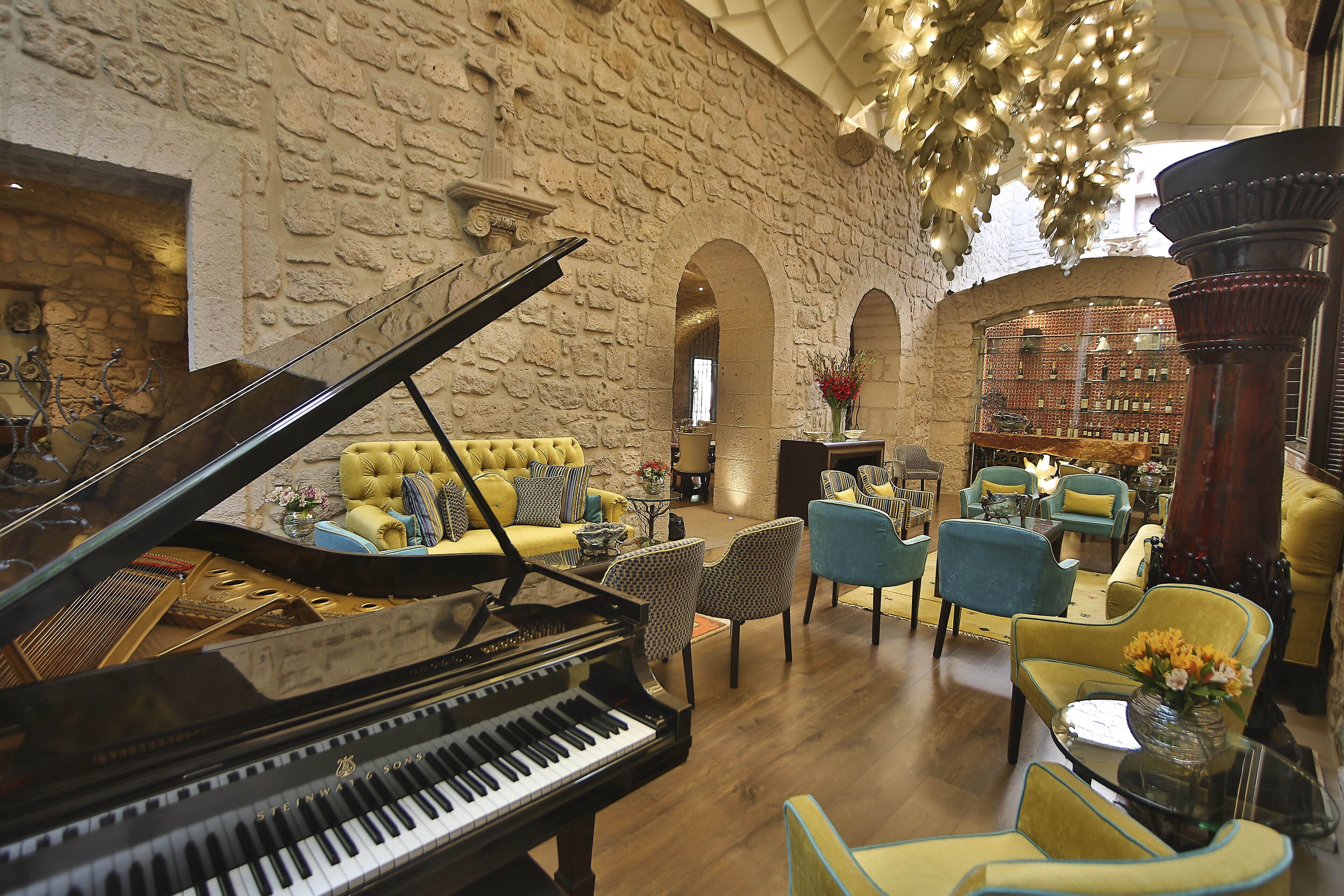 A grand piano in a spacious, well-lit room with a stone wall, comfortable seating, and a chandelier.