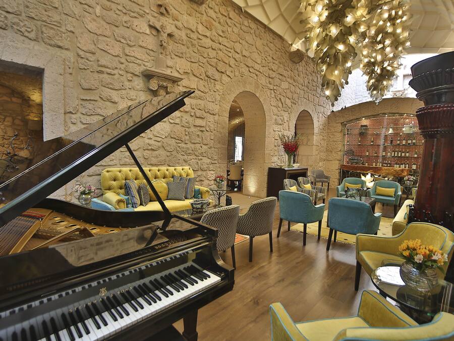 A grand piano in a spacious, well-lit room with a stone wall, comfortable seating, and a chandelier.