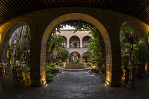Ein Innenhof mit Steinbögen, einer zentralen Fontäne und Tischen mit Stühlen zum Essen.