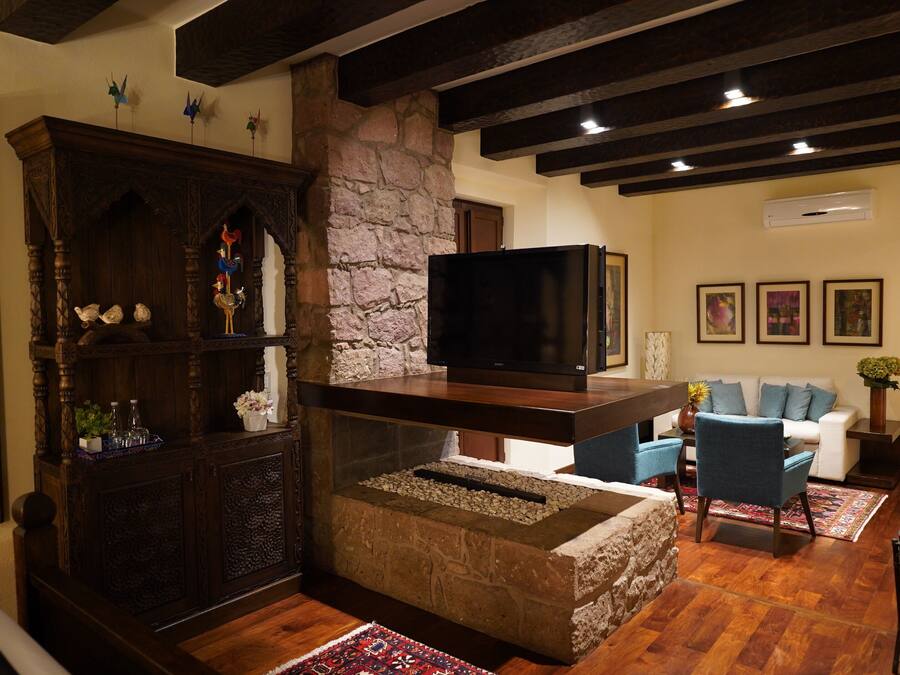 A cozy living room with a stone fireplace, wooden furniture, a flat-screen TV, and a stone wall.