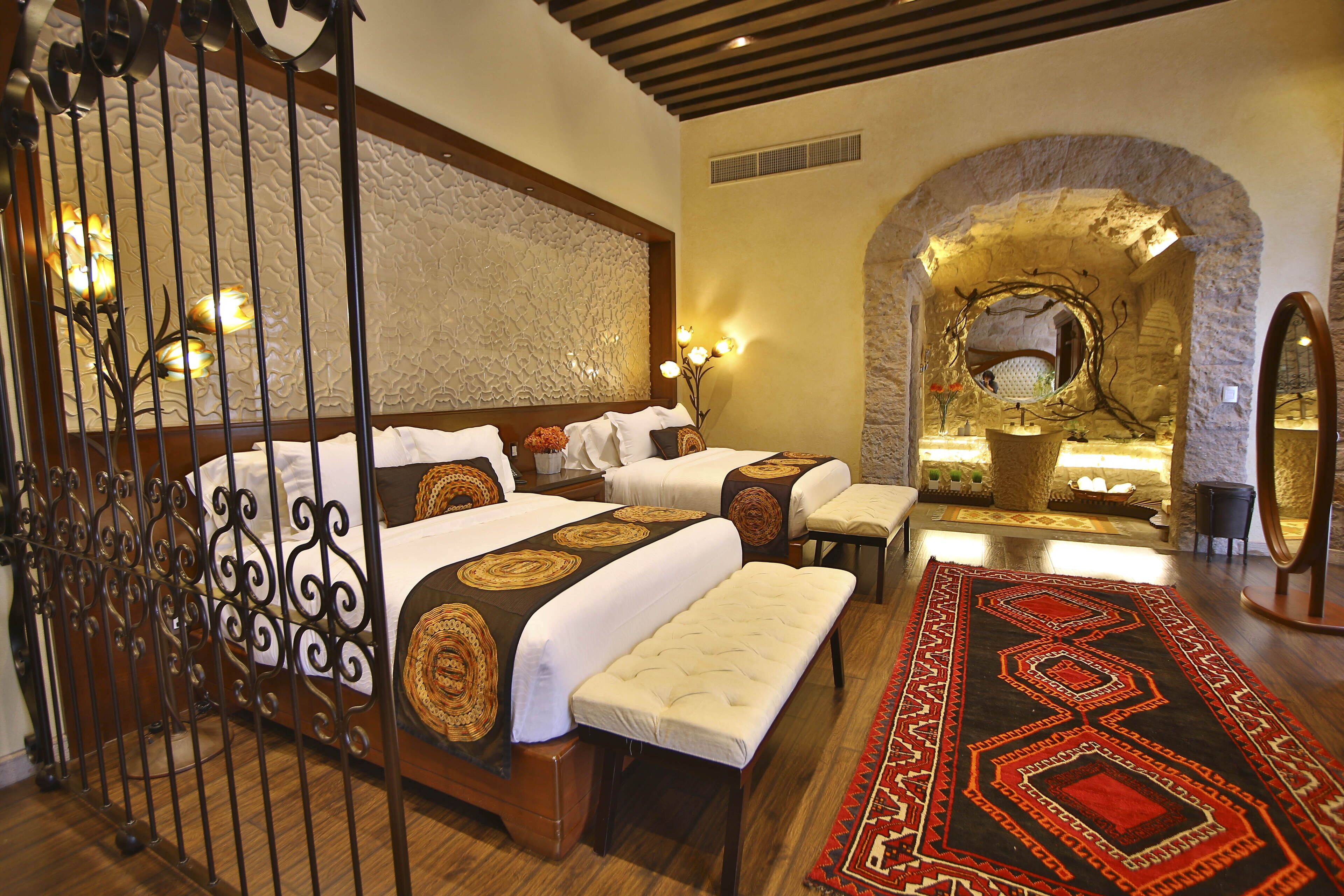 Habitación de hotel con dos camas, un banco, un tapete decorativo y un arco de piedra.