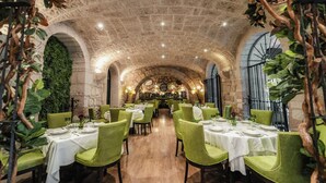 Un restaurante con arcos de piedra, sillas verdes y manteles blancos.