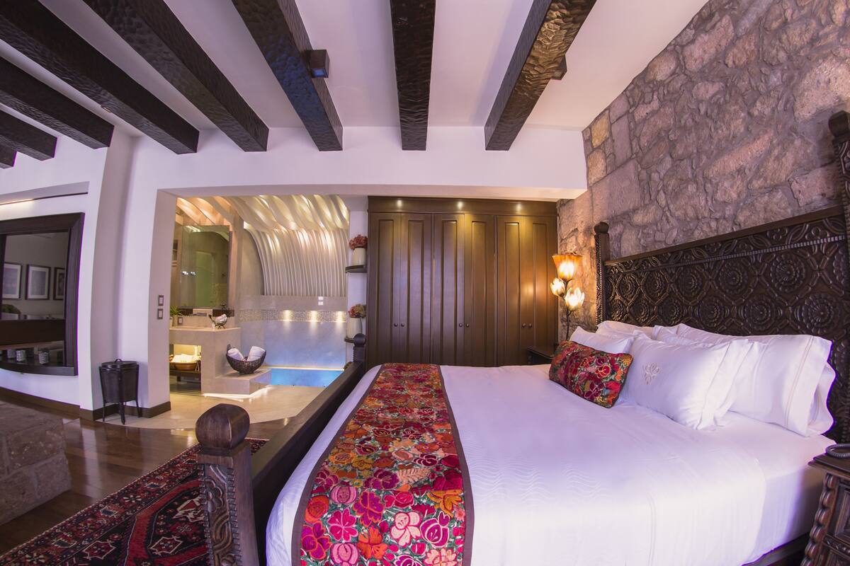 A spacious bedroom with a large bed, a stone accent wall, and a built-in bathtub.