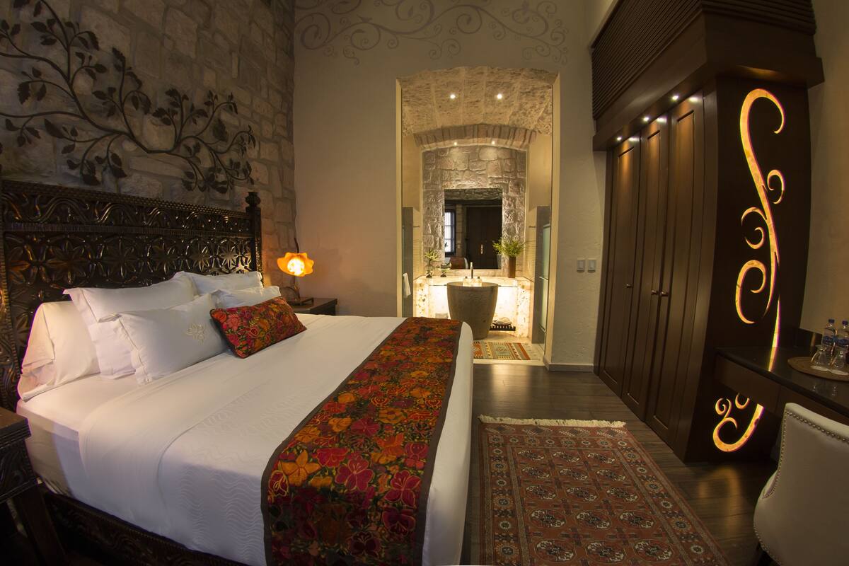 A bedroom with a large bed, a nightstand, a dresser, and a bathroom visible through an archway.