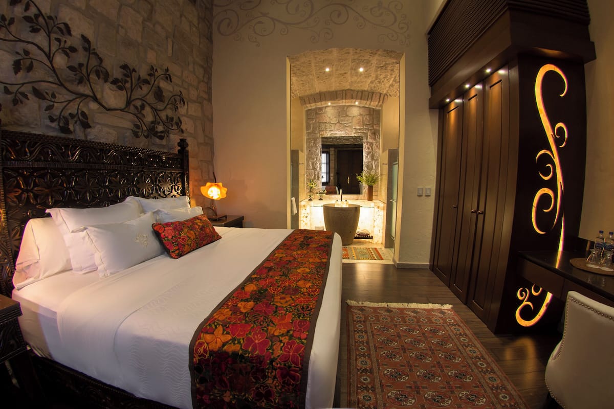 Un dormitorio con una cama grande, una mesita de noche, un aparador y un baño visible a través de un arco.